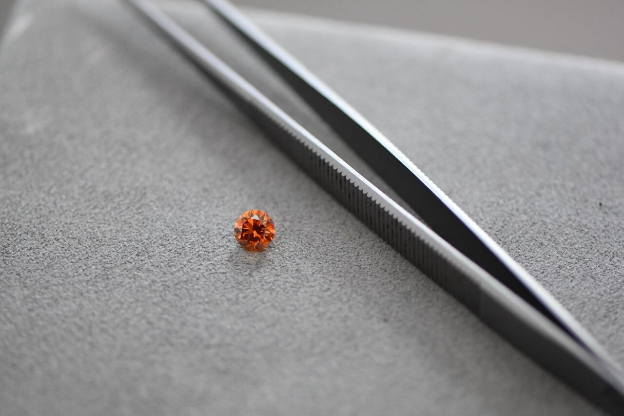 Natürlicher Fancy Color Diamant mit intensiver oranger Farbwirkung neben Pinzette