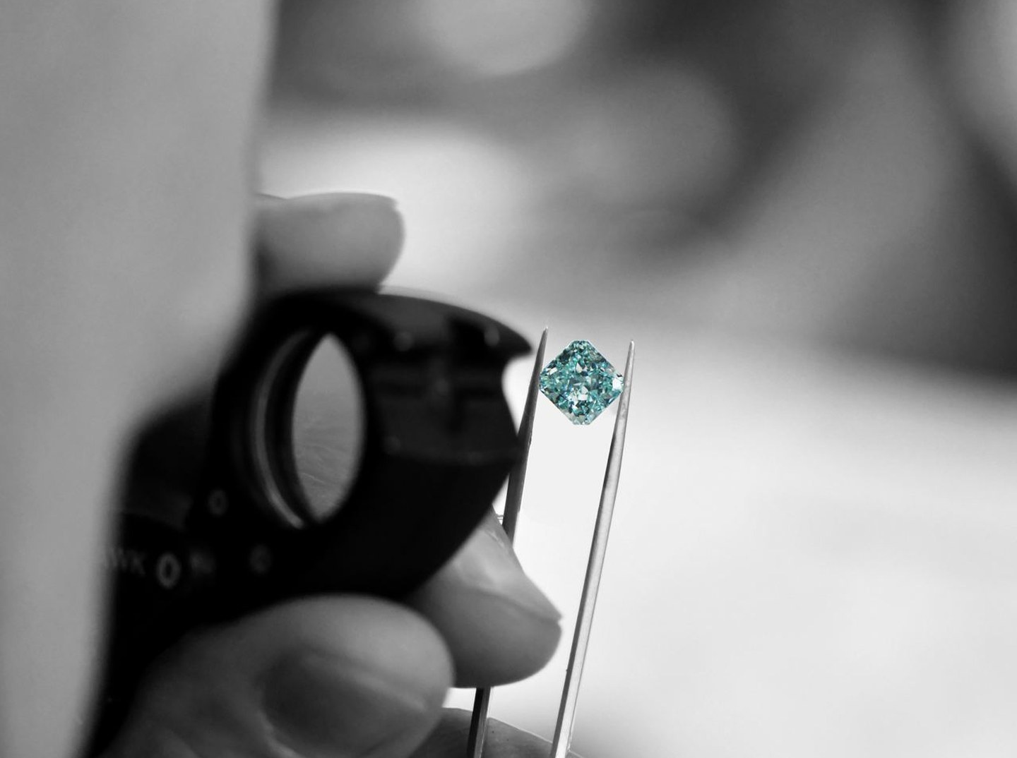 Ein natürlicher Fancy Color Diamant in der Zange, daneben die Einschlaglupe