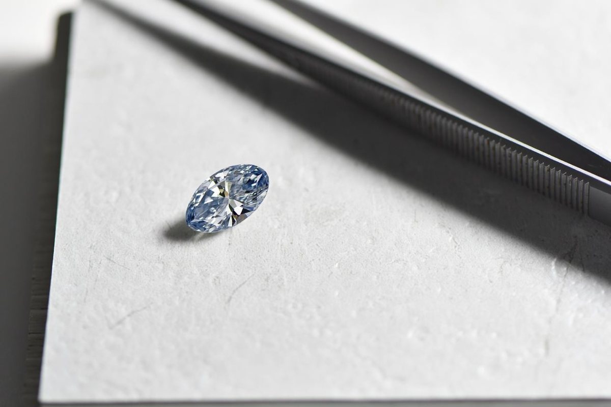 Natürlicher Fancy Blue Diamant im Marquise Schliff mit Pinzette auf heller Arbeitsunterlage