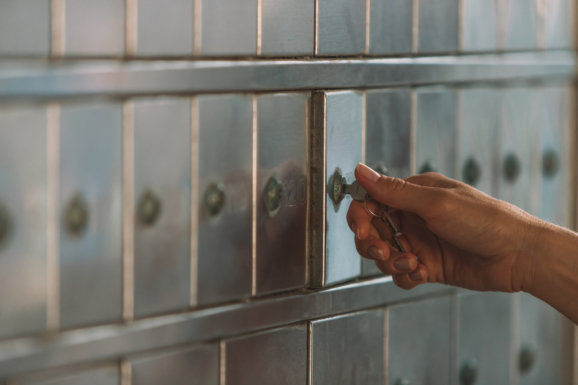 Close-up of a female hand opening a mailbox with a small key - post office box or PO BOX concept - bank deposit box